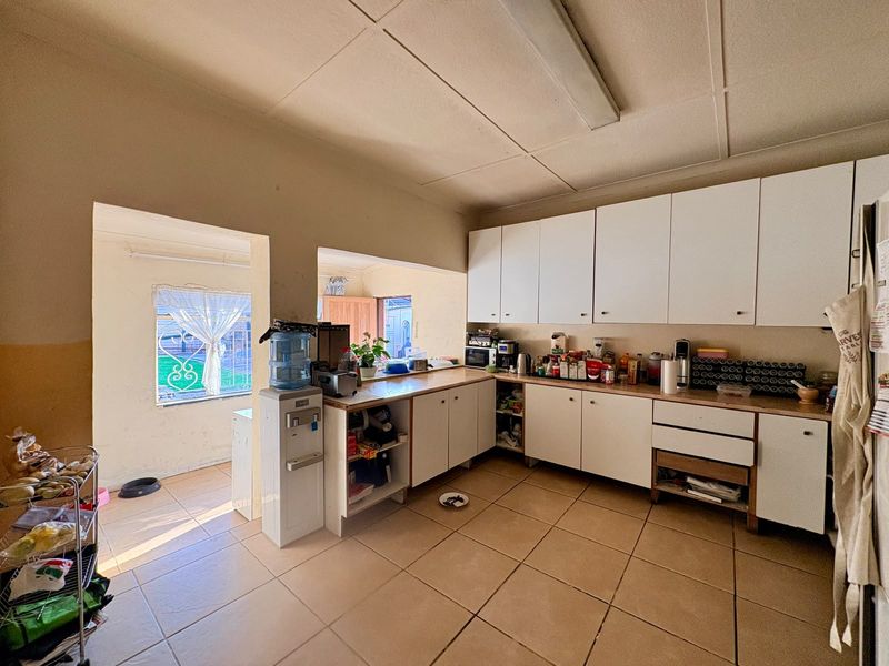 A functional kitchen featuring white cabinetry, laminate countertops, and tiled flooring, with an adjacent utility area and direct access to the exterior.