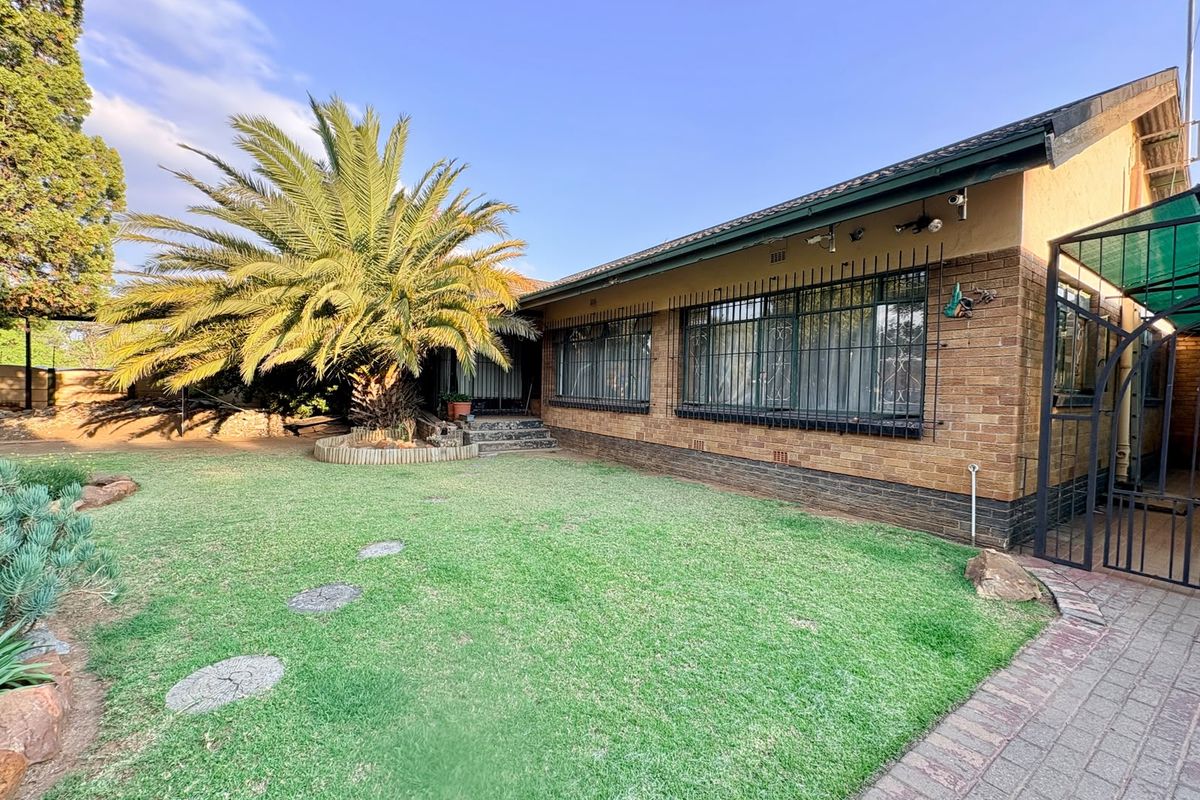 A well-maintained rear exterior view of a brick house featuring a spacious lawn, mature palm tree, and secure window bars.