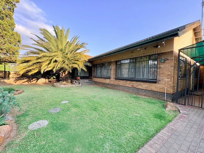 A well-maintained rear exterior view of a brick house featuring a spacious lawn, mature palm tree, and secure window bars.
