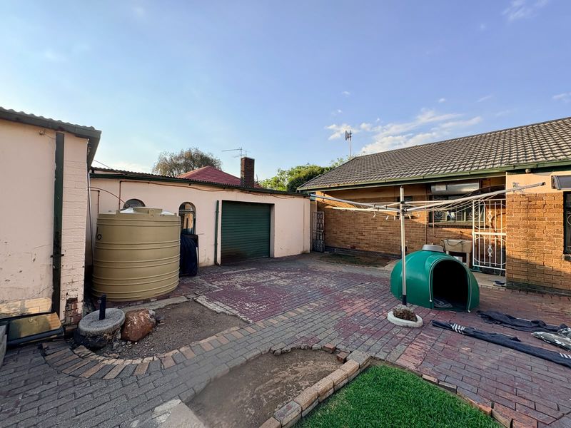 Rear exterior view showing a paved courtyard area, water storage tank, and access to the garage and main dwelling structure.