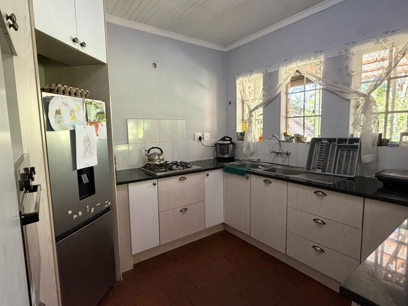 Functional kitchen featuring light-toned cabinetry, dark countertops, a gas hob, and a double sink with natural light from multiple windows.
