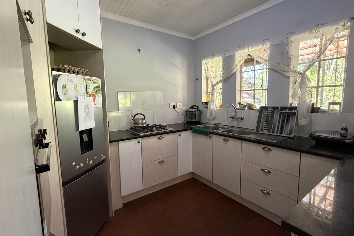 Functional kitchen featuring light-toned cabinetry, dark countertops, a gas hob, and a double sink with natural light from multiple windows.