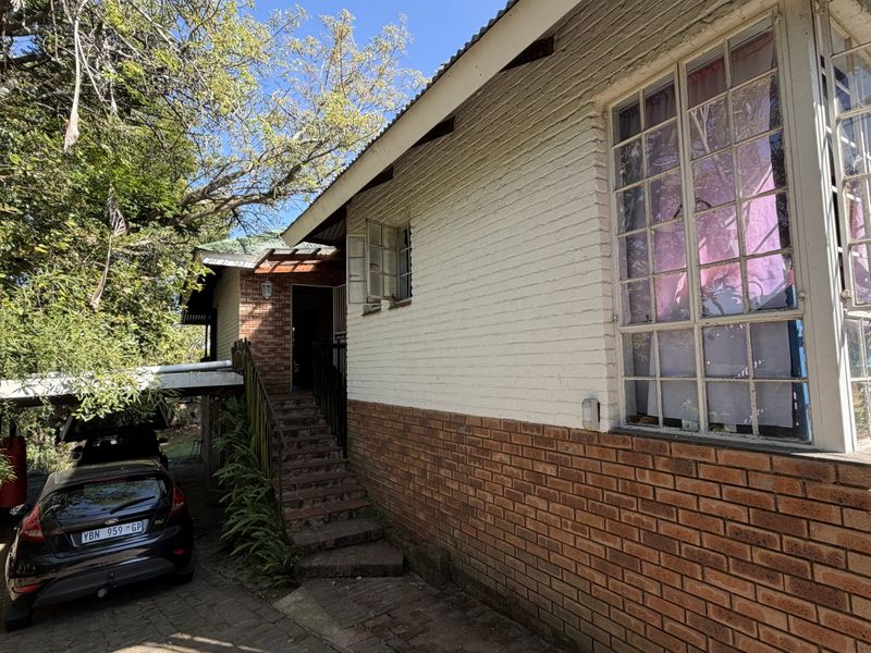 Side view of the property featuring a brick facade, steel-framed windows, concrete stairs leading to the entrance, and a covered carport area.