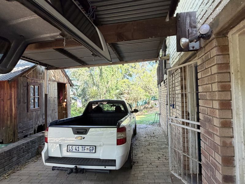 A covered outdoor parking area featuring brick walls, paved flooring, and a corrugated metal roof structure.