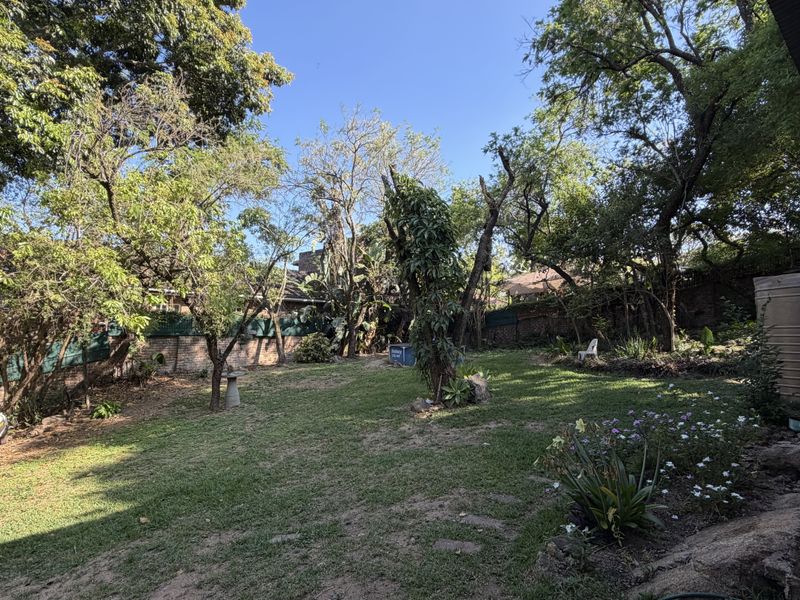 A spacious, established garden featuring mature trees, a brick boundary wall, and a water tank, offering a private outdoor setting.