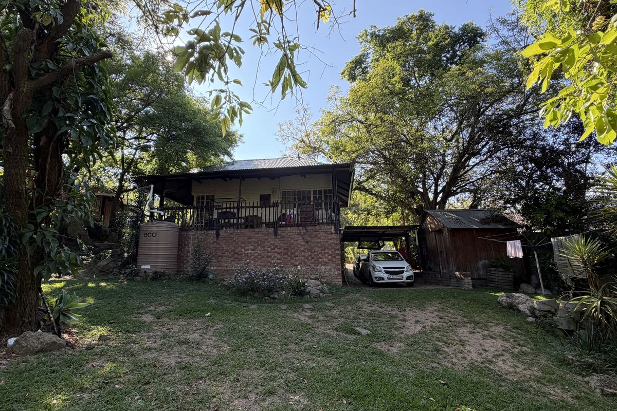 Rear view of the property featuring a raised covered patio, brick foundation, water storage tank, and a detached timber shed set in a garden.