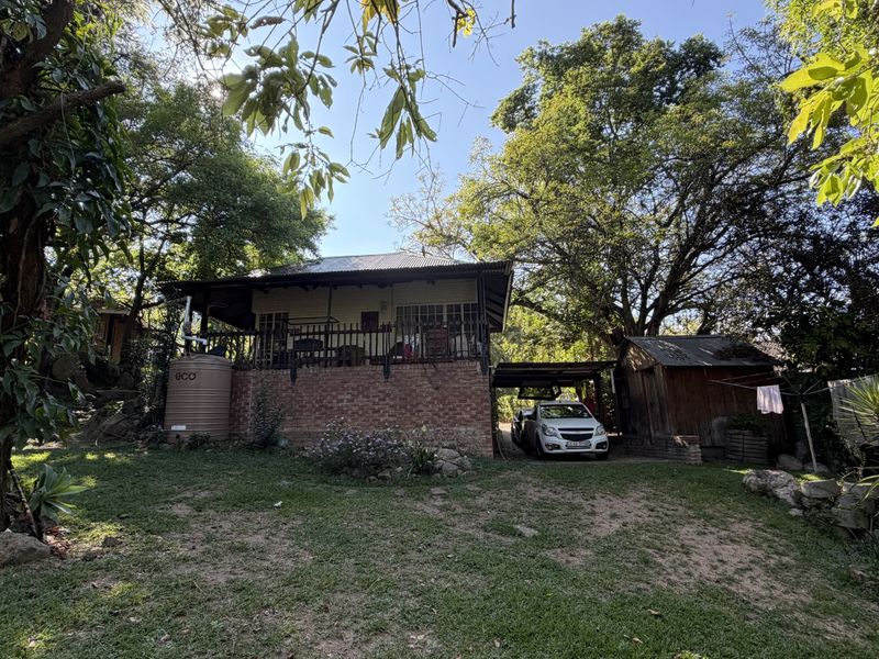 Rear view of the property featuring a raised covered patio, brick foundation, water storage tank, and a detached timber shed set in a garden.