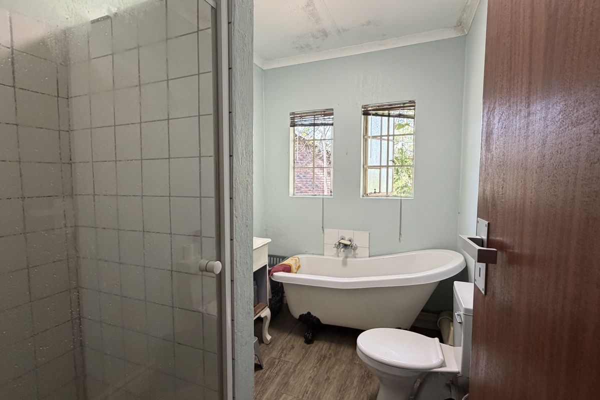 A dated bathroom featuring a freestanding bathtub, separate shower enclosure, and toilet, requiring cosmetic updates to the ceiling and finishes.