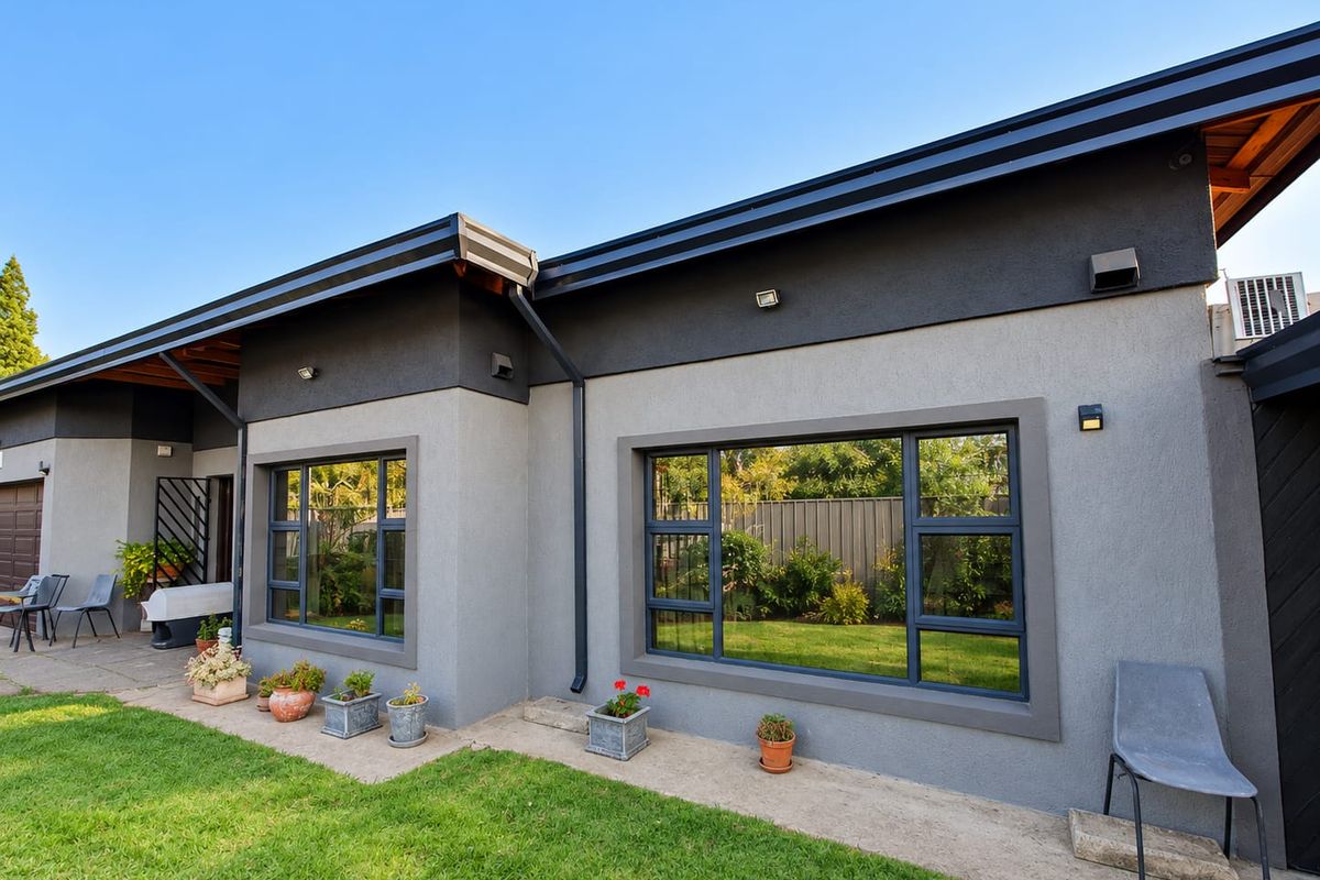 Rear exterior view of the house featuring modern grey rendered walls, dark aluminium window frames, and a well-maintained garden pathway.