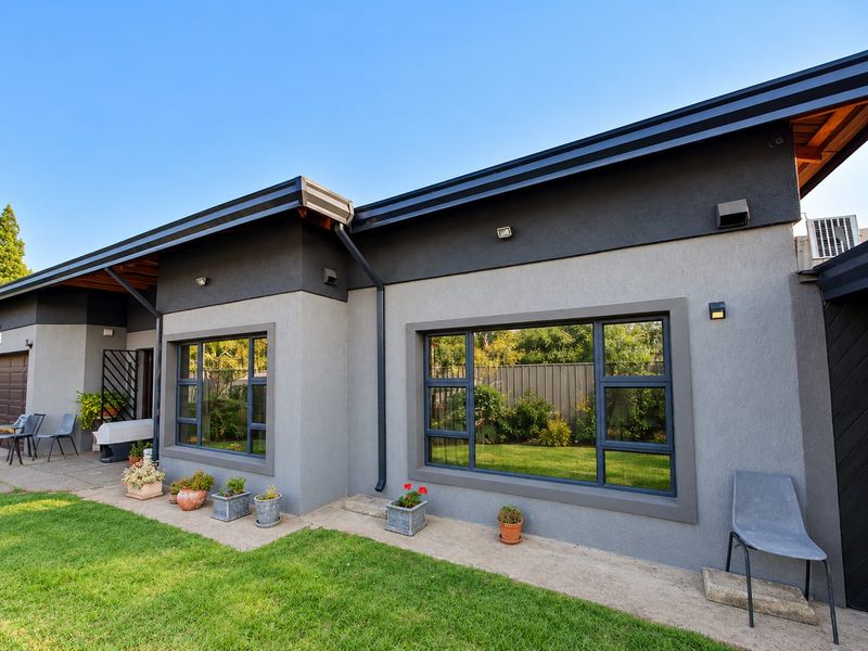 Rear exterior view of the house featuring modern grey rendered walls, dark aluminium window frames, and a well-maintained garden pathway.