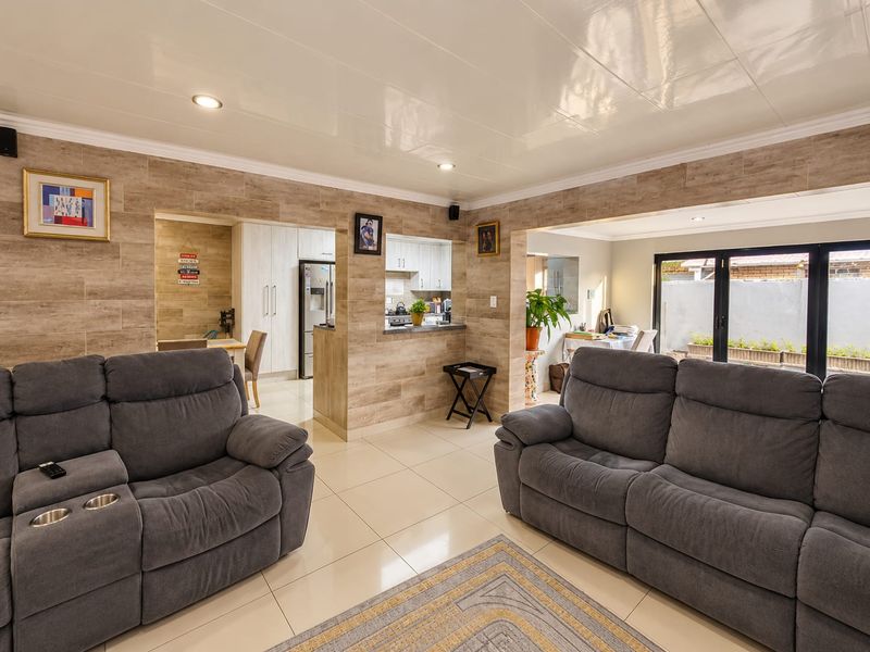 Spacious open-plan living area featuring tiled floors, stone-look wall accents, recessed lighting, and seamless flow to the kitchen and outdoor patio area.