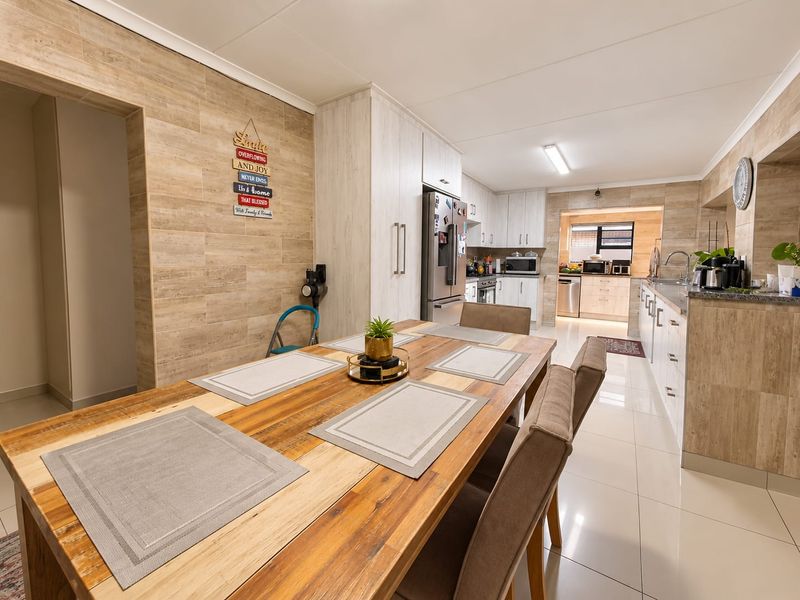 Modern open-plan kitchen and dining area featuring sleek cabinetry, stone countertops, tiled flooring, and a stylish feature wall.
