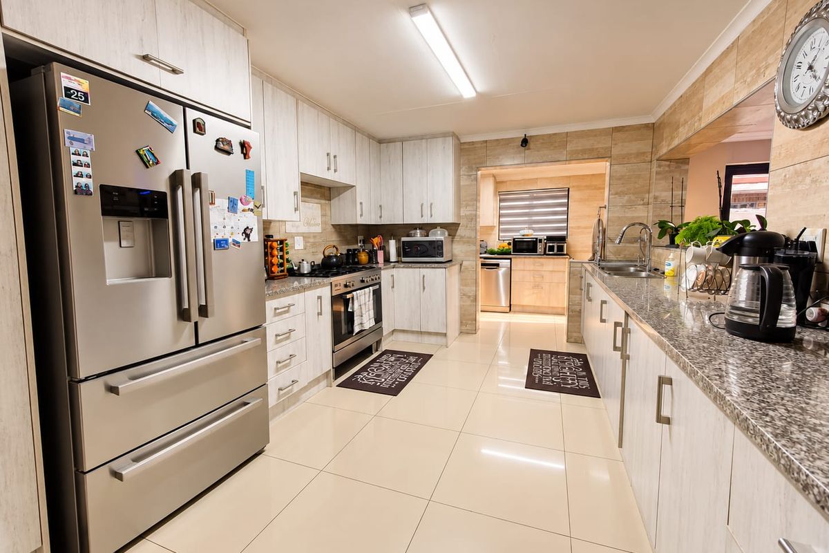 Modern kitchen featuring light wood-grain cabinetry, granite countertops, stainless steel appliances, and a seamless transition into a secondary scullery area.