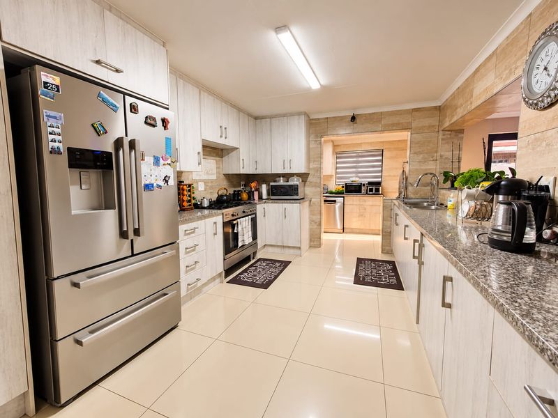 Modern kitchen featuring light wood-grain cabinetry, granite countertops, stainless steel appliances, and a seamless transition into a secondary scullery area.