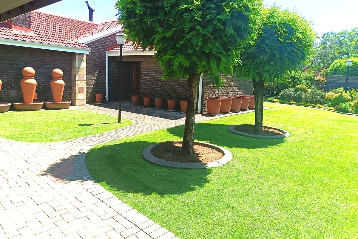 A well-maintained rear garden featuring a brick facade, paved pathways, and manicured lawn with established trees.