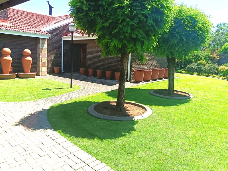 A well-maintained rear garden featuring a brick facade, paved pathways, and manicured lawn with established trees.