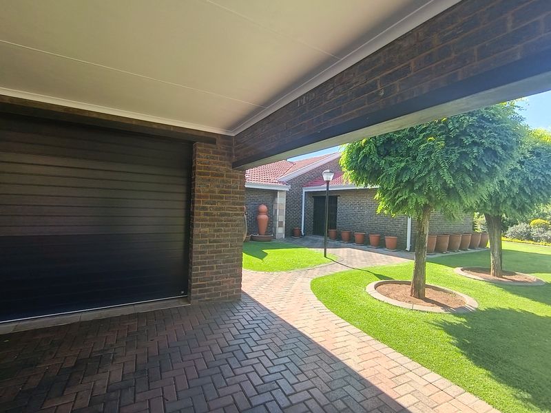 A well-maintained front exterior featuring a brick facade, paved driveway, covered carport, and a neatly landscaped garden with a paved walkway.