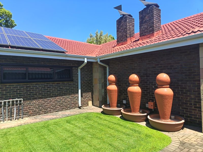 Rear exterior view featuring a brick facade, tiled roof with solar panels, and a paved patio area with decorative water features.