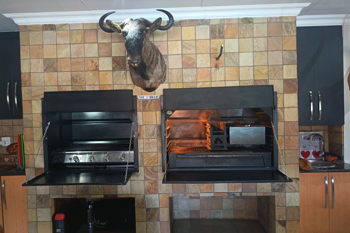 Indoor entertainment area featuring a dual built-in braai setup with stone tile cladding, integrated cabinetry, and a sink.