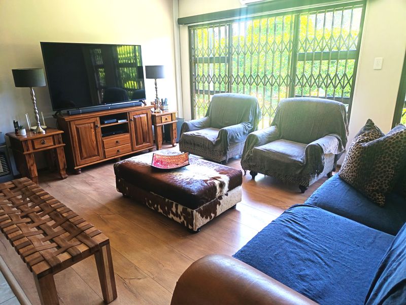 A comfortable living room featuring laminate flooring, a sliding glass door with security gate, and an integrated air conditioning unit.