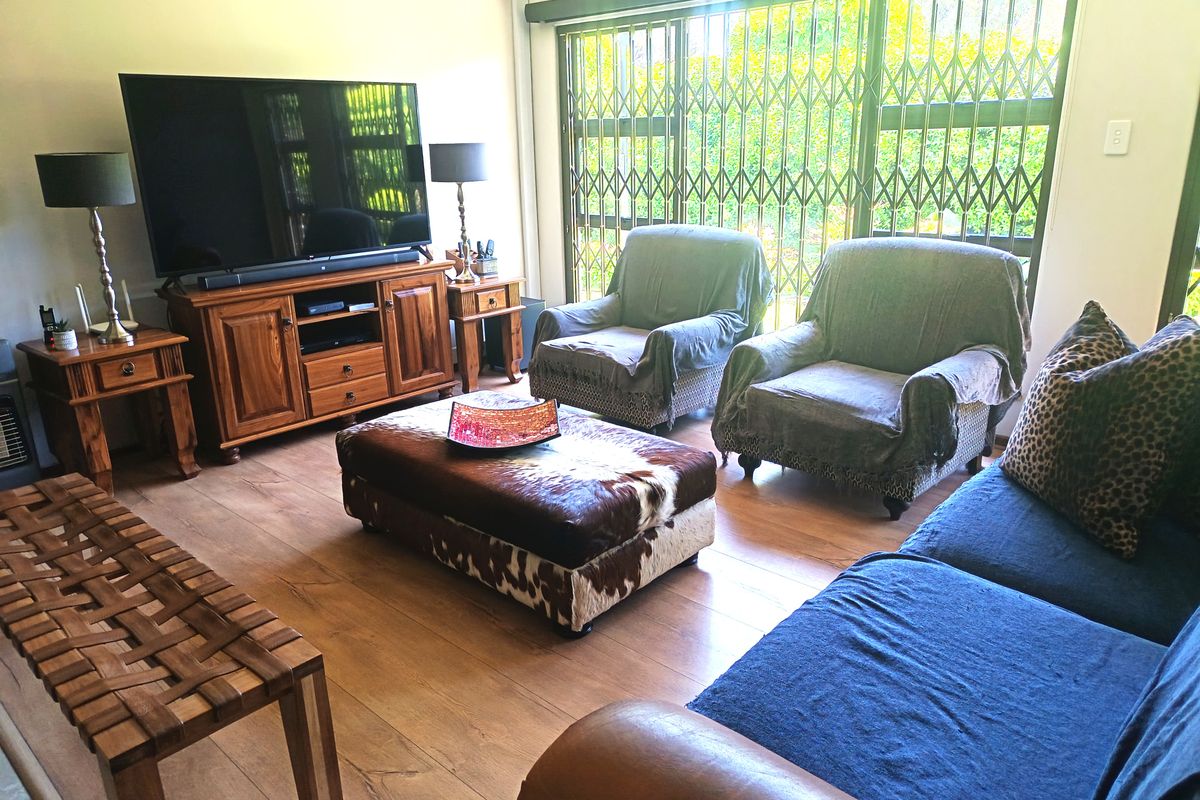 A comfortable living room featuring laminate flooring, a sliding glass door with security gate, and an integrated air conditioning unit.