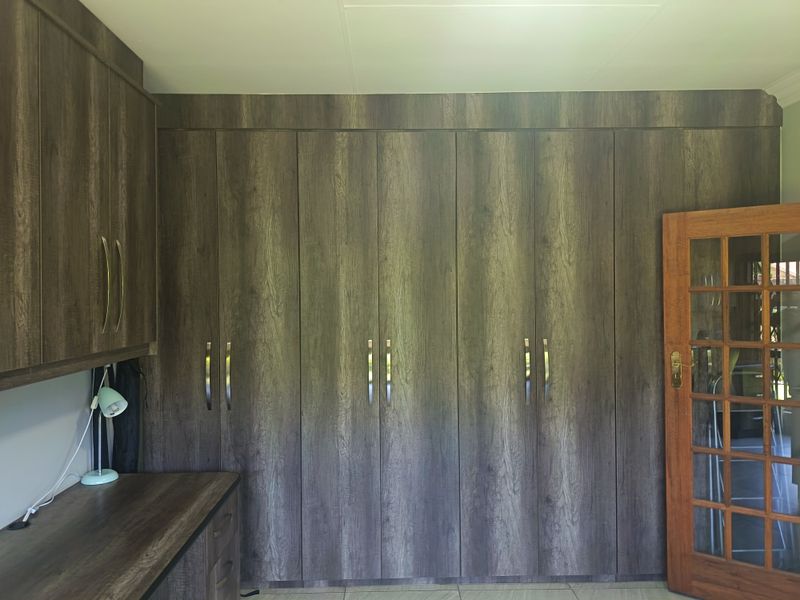 A bedroom featuring extensive built-in cupboards with a wood-grain finish, a matching built-in desk, and a classic timber-framed glass door.