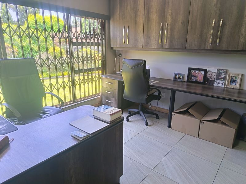 A functional home office featuring built-in desk space, ample overhead cabinetry, tiled flooring, and a large window with a security gate.