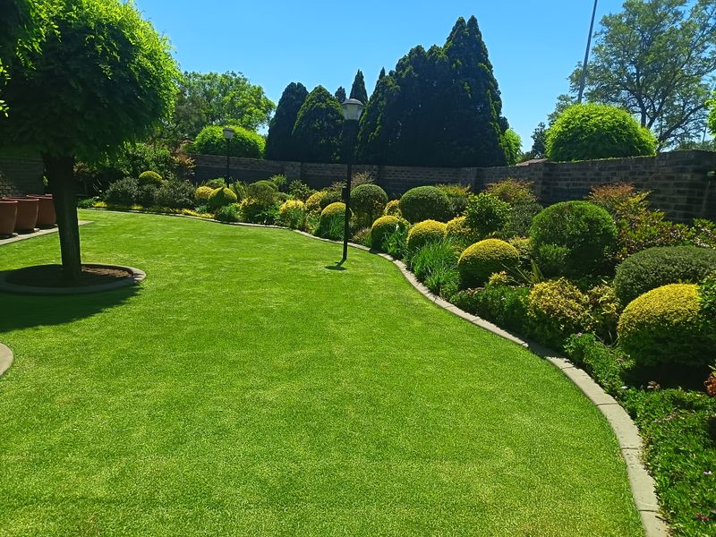 A well-maintained garden featuring a manicured lawn, structured shrubbery, brick boundary walls, and integrated garden lighting.