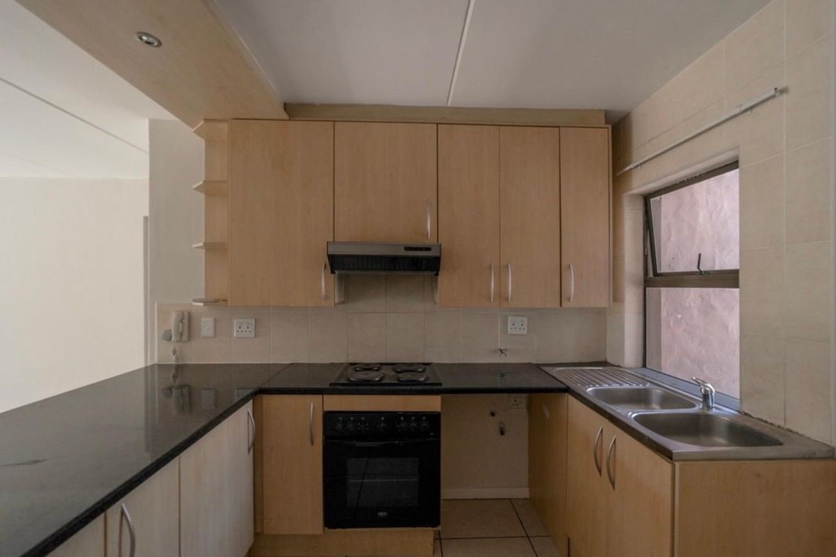 A functional kitchen featuring light wood cabinetry, granite countertops, a built-in oven with hob, and a stainless steel double sink.