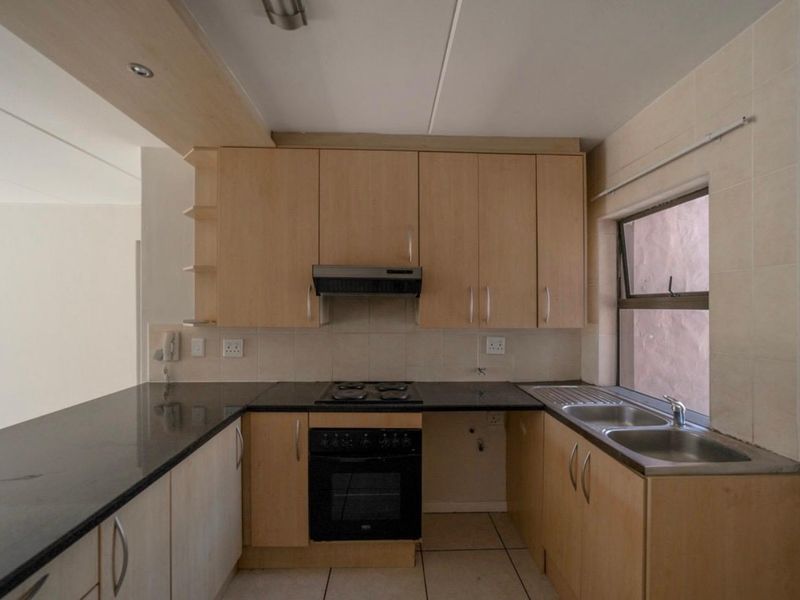 A functional kitchen featuring light wood cabinetry, granite countertops, a built-in oven with hob, and a stainless steel double sink.