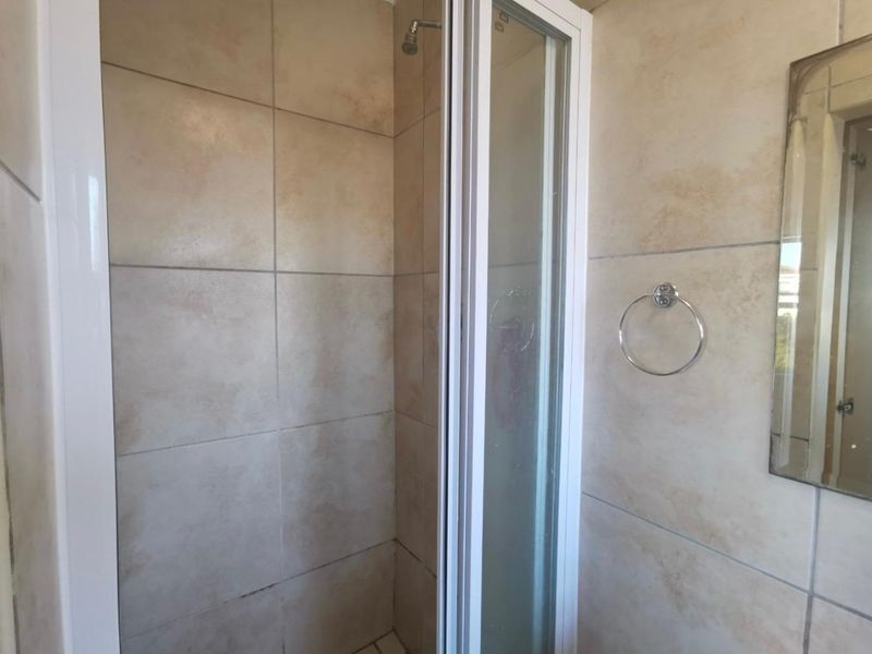A functional bathroom shower area featuring neutral wall tiling, a glass shower enclosure, and a wall-mounted towel ring.