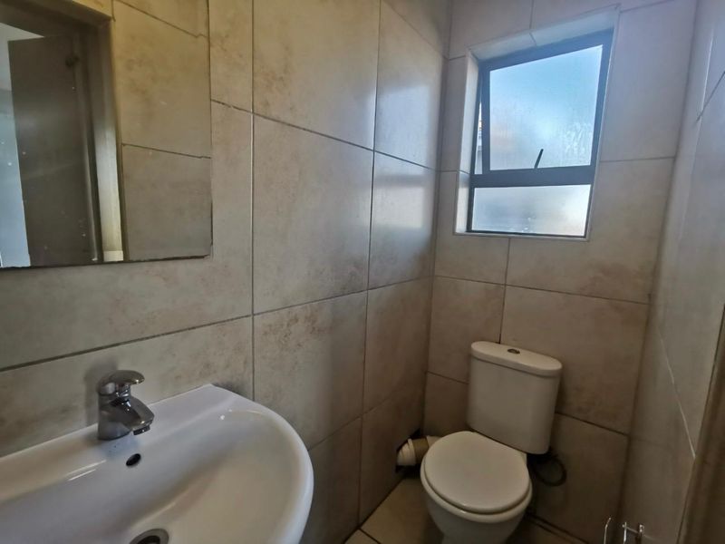 A compact bathroom featuring neutral ceramic wall tiles, a pedestal basin with chrome mixer, and a standard toilet.