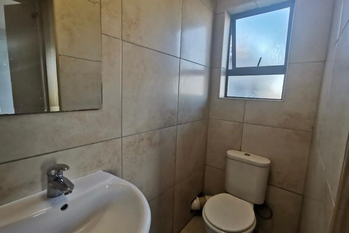 A compact bathroom featuring neutral ceramic wall tiles, a pedestal basin with chrome mixer, and a standard toilet.