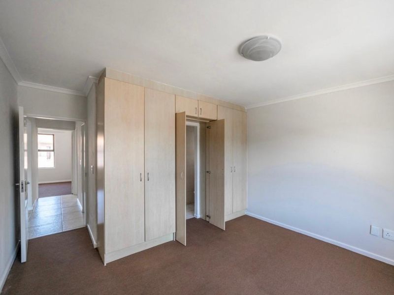 A clean, empty bedroom featuring light wood-finish built-in cupboards, neutral walls, and carpeted flooring, offering a versatile space ready for personalization.