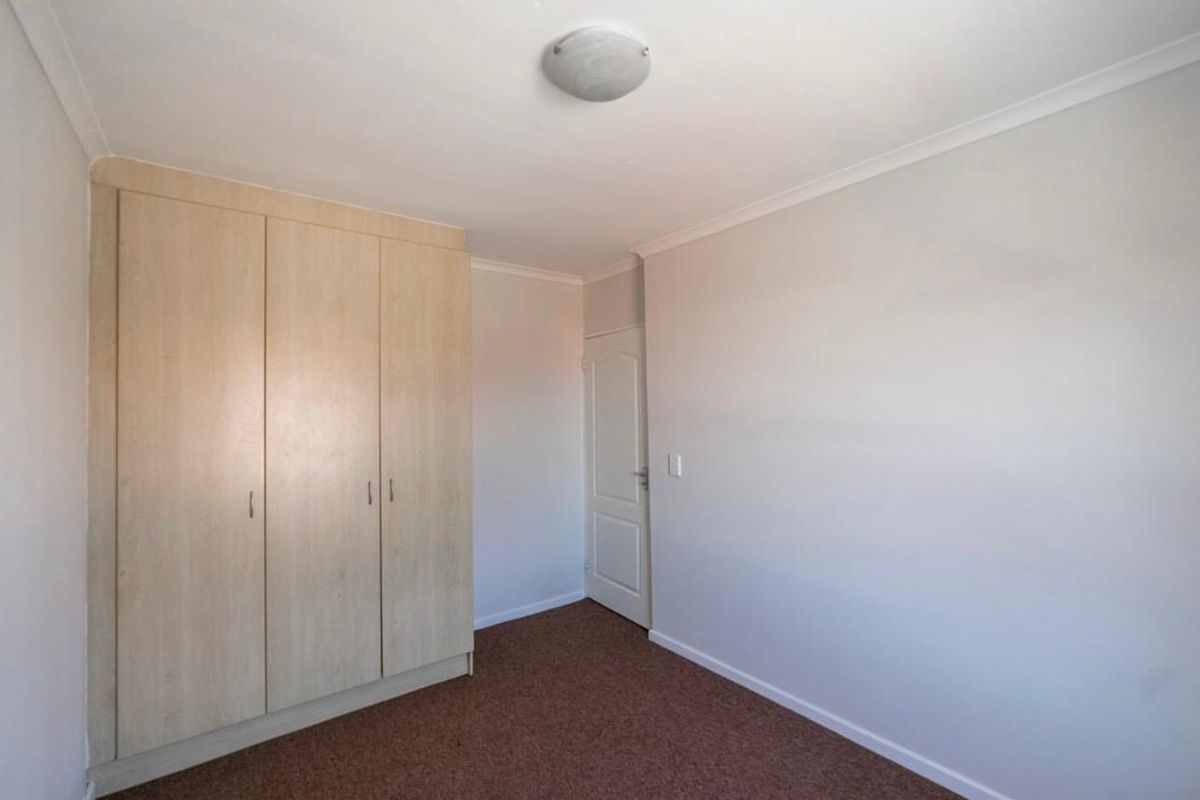 A clean, empty bedroom featuring neutral walls, carpeted flooring, and built-in wooden cupboards, offering a blank canvas for personalization.