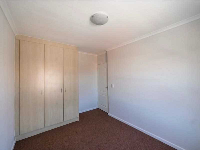 A clean, empty bedroom featuring neutral walls, carpeted flooring, and built-in wooden cupboards, offering a blank canvas for personalization.