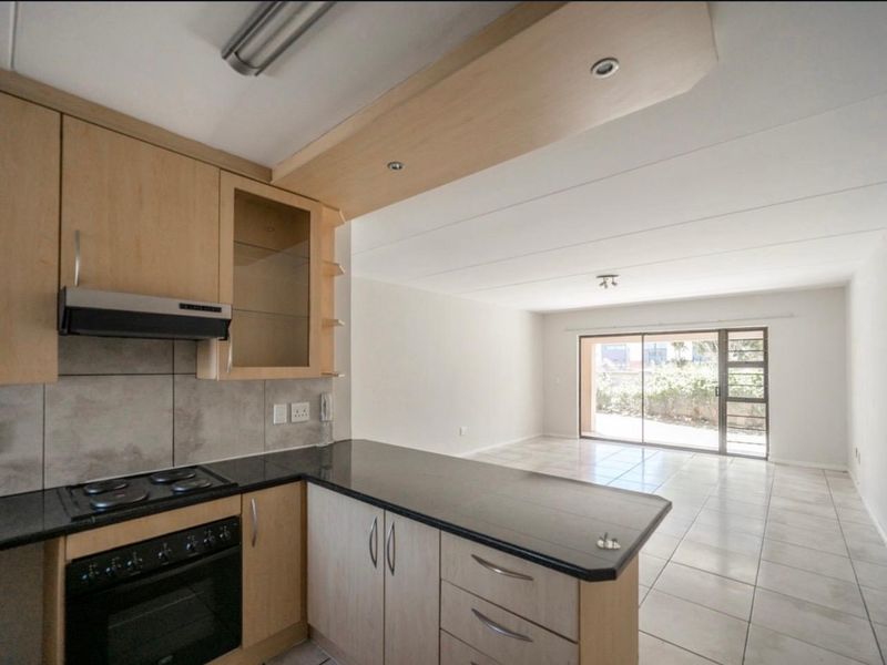 Open-plan kitchen and living area featuring light wood cabinetry, granite countertops, tiled floors, and sliding glass doors leading to an outdoor space.