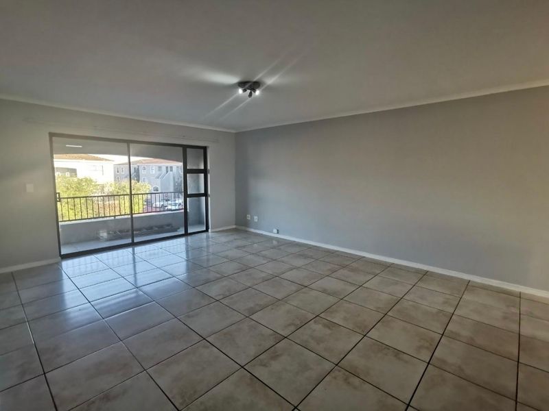 Spacious, empty living room featuring neutral tiled flooring, grey walls, and a large sliding glass door providing access to an outdoor balcony.