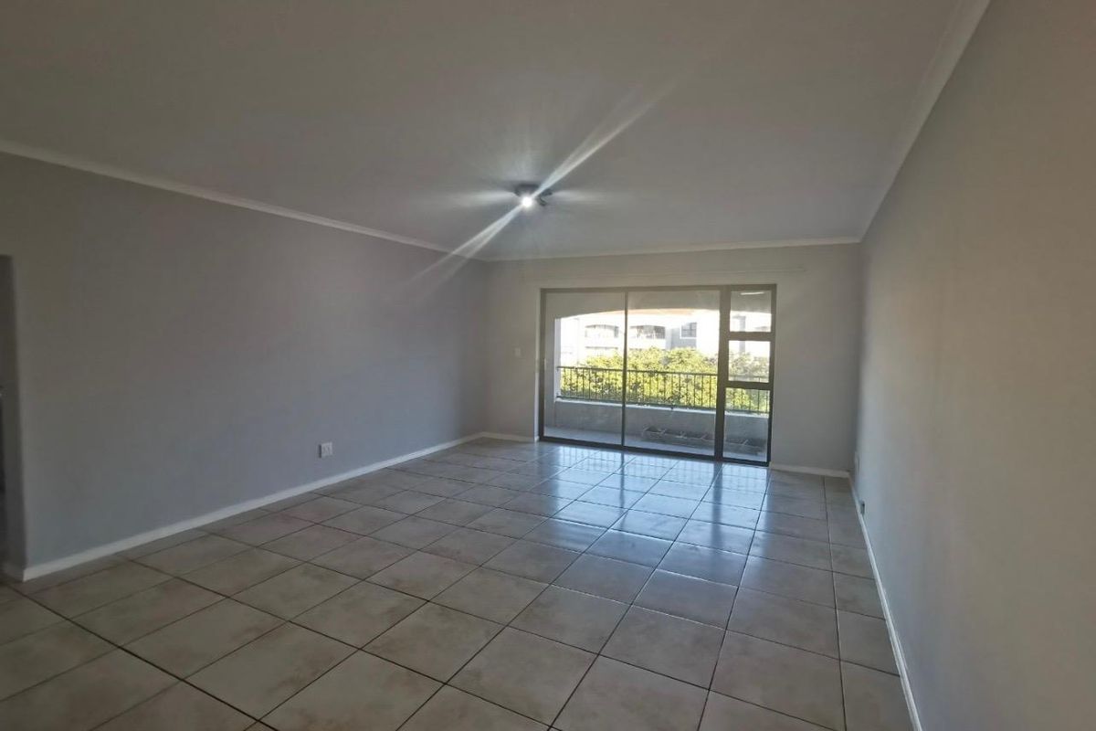 A spacious, empty living room featuring neutral grey walls, ceramic floor tiles, and a large sliding glass door providing access to a balcony.