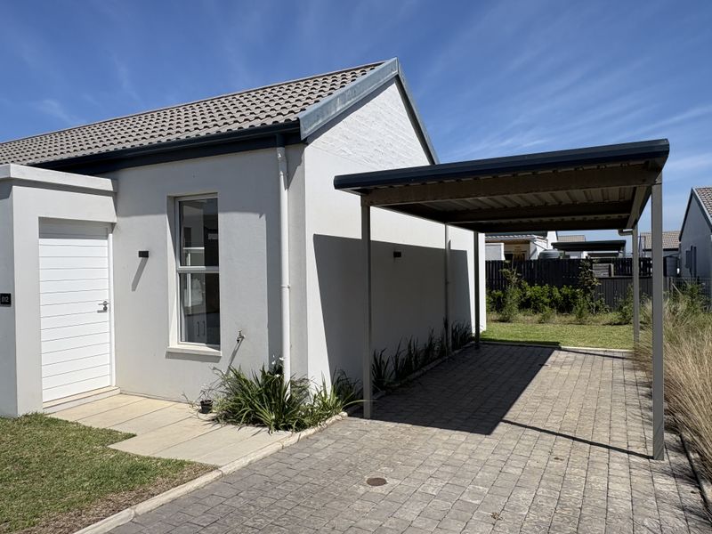 Front elevation of a modern cluster home featuring a paved driveway, covered carport, and a clean, well-maintained exterior facade.