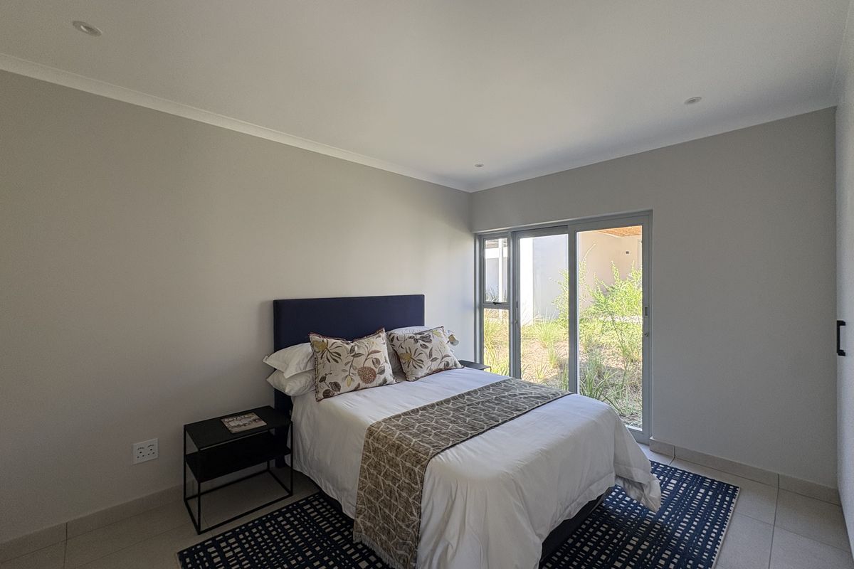 A bright bedroom featuring neutral walls, tiled flooring, recessed lighting, and a sliding glass door providing direct access to the garden area.