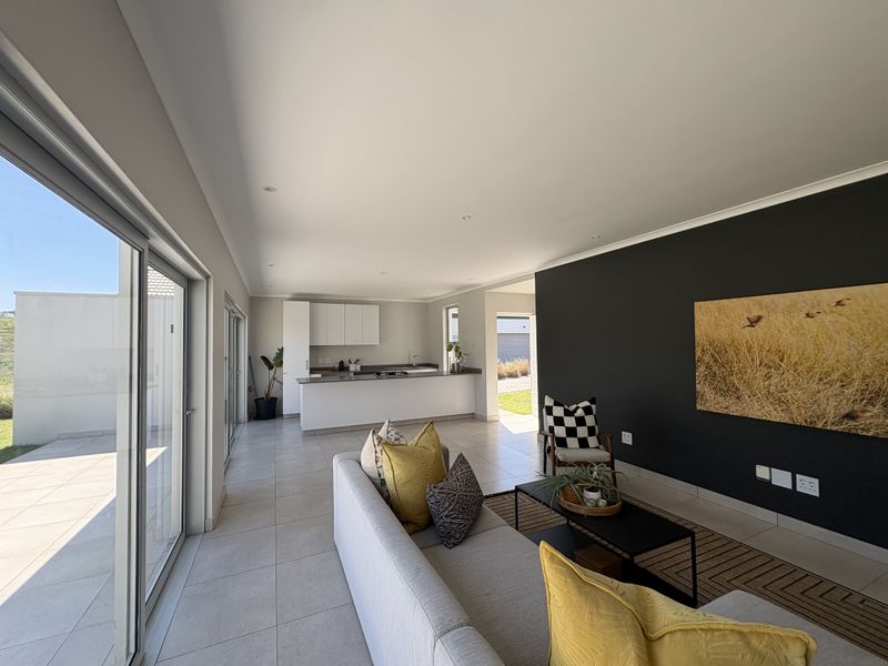 Modern open-plan living area featuring tiled floors, recessed lighting, and a sleek kitchen with a central island, seamlessly connected to an outdoor patio.