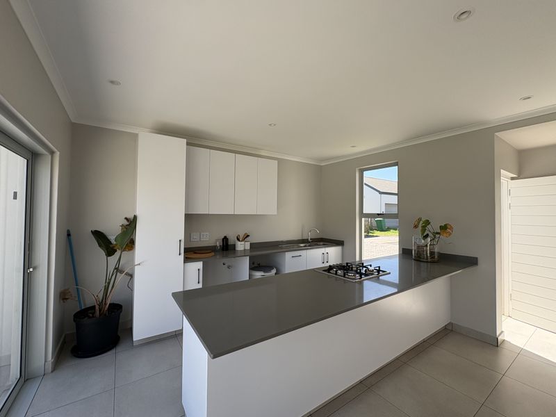 Modern kitchen featuring white cabinetry, stone countertops, a central island with a gas hob, and tiled flooring in a bright, open-plan layout.