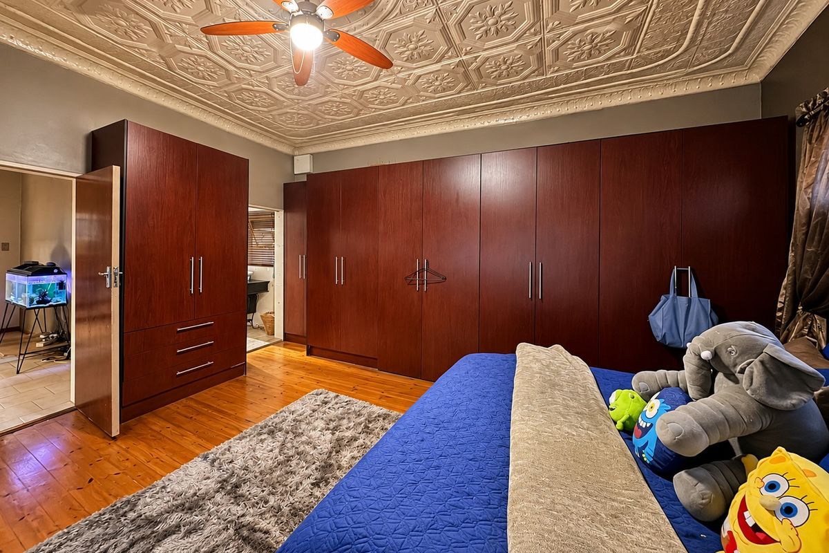 Spacious bedroom featuring extensive built-in cabinetry, a decorative pressed metal ceiling, a ceiling fan, and polished hardwood flooring.