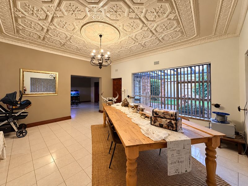 Spacious dining room featuring a distinctive ornate coffered ceiling, tiled flooring, and large windows with security bars overlooking the garden.