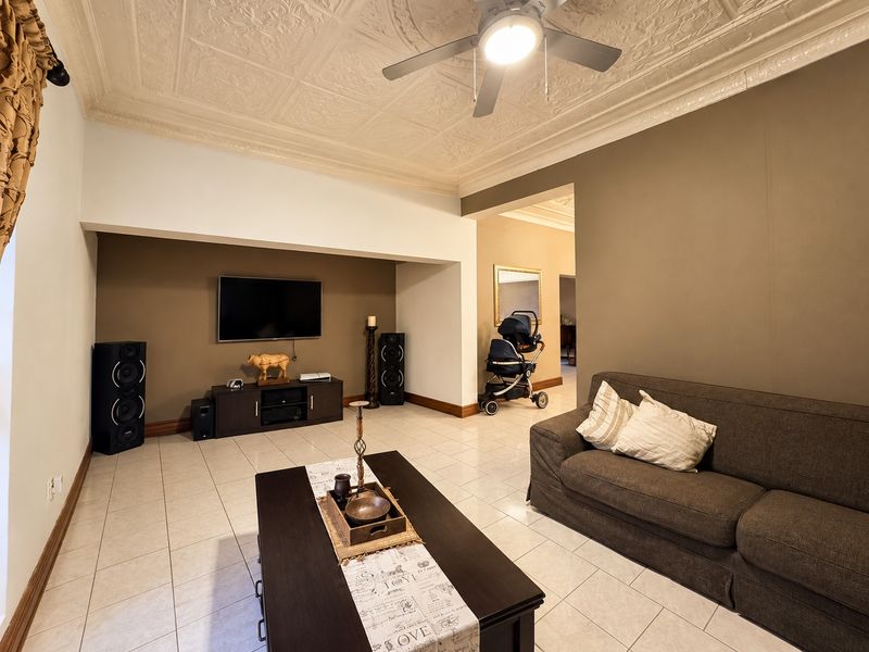 Spacious living room featuring a decorative pressed metal ceiling, ceiling fan, and neutral tiled flooring, offering a comfortable and well-maintained living space.