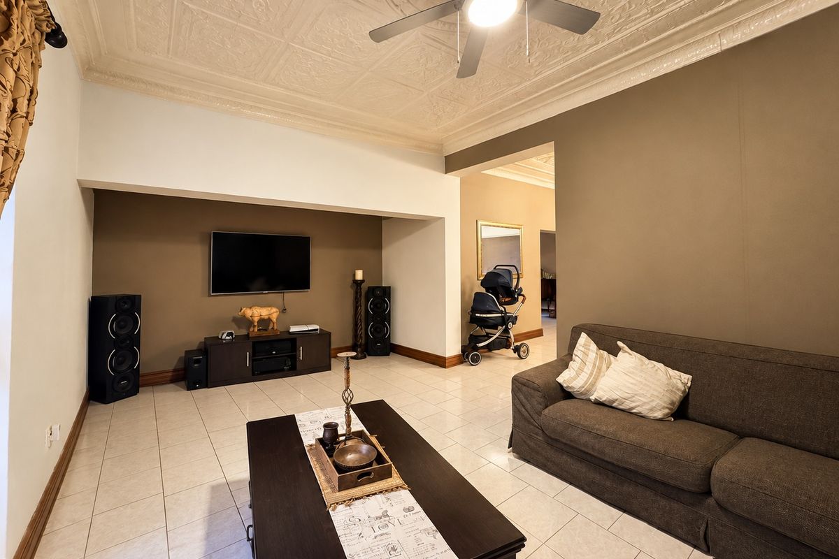 Spacious living room featuring a decorative pressed metal ceiling, ceiling fan, and neutral tiled flooring, offering a comfortable and well-maintained living space.