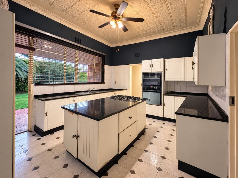 Spacious kitchen featuring a central island, built-in oven, gas cooktop, and classic pressed metal ceilings, with direct access to the outdoor garden area.