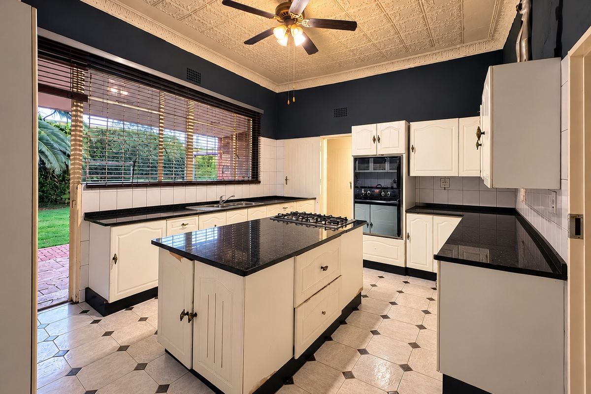 Spacious kitchen featuring a central island, built-in oven, gas cooktop, and classic pressed metal ceilings, with direct access to the outdoor garden area.