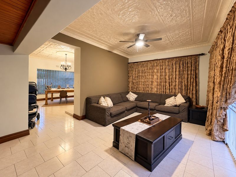 Spacious open-plan living area featuring a decorative pressed metal ceiling, ceiling fan, and neutral tiled flooring, seamlessly connecting to the adjacent dining space.